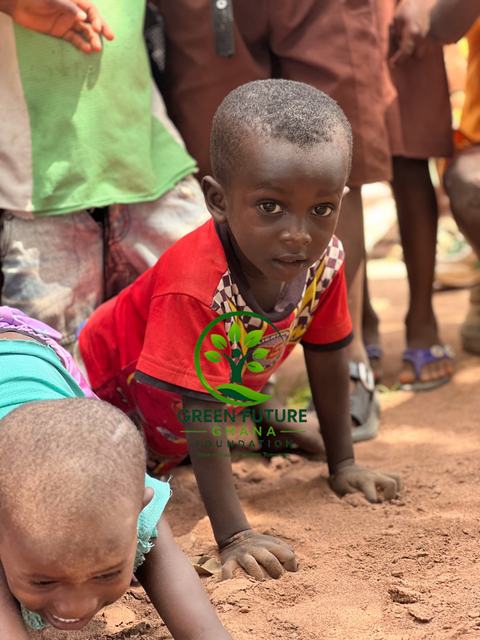 A smiling boy in a red shirt crouching on the ground