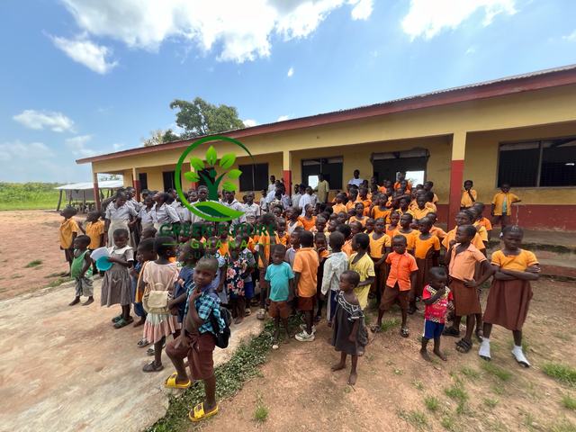 Pupils lined up in the schoolyard along a yellow and red school building