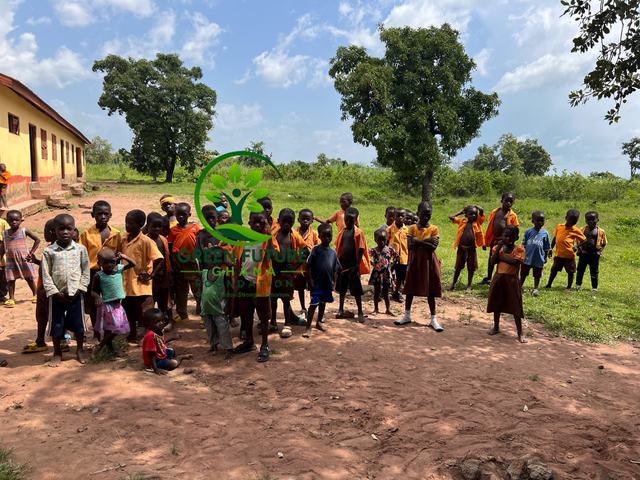 A group of pupils standing in a field near their school and large trees