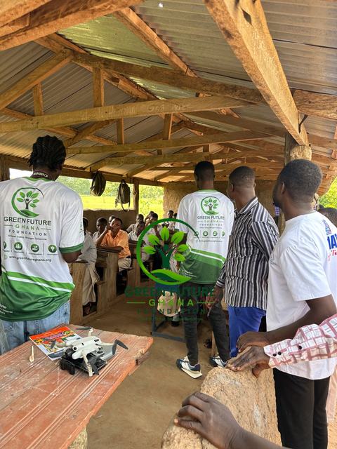 Volunteers gathered around a table with a small drone under an open wooden shelter
